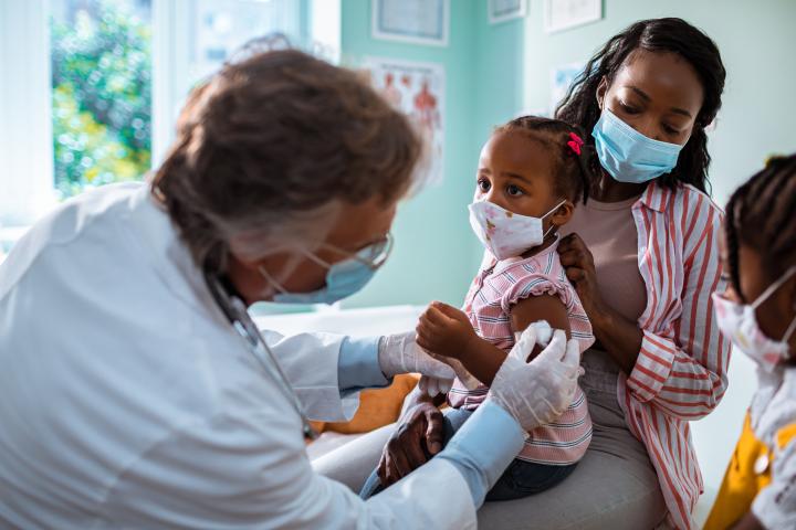 A photo of a mother and two children in a doctor's office where one child is being vaccinated
