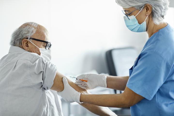A photograph of a female nurse vaccinates an older man against covid-19