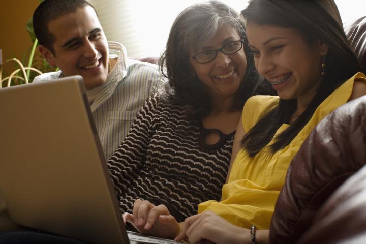 A mother sitting in the middle of her son and daughter with a laptop laughing.