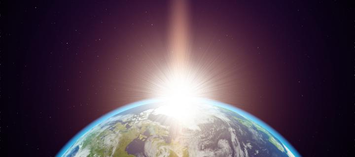 A view of the Earth from space with a flare of sunlight appearing on the horizon.