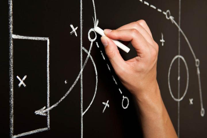 Photo of a man's hand using chalk to solve a problem on a blackboard