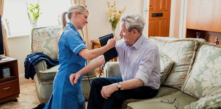 A female nurse checks the blood pressure of a senior man whilst visiting him on a house call