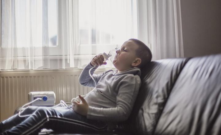 Young boy sat on sofa using breathing equipment with mask