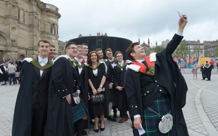 10 students in graduation gowns smiling and taking a selfie outside McEwan Hall