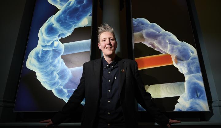 Professor Susan Rosser poses in front of an image render of a DNA molecule