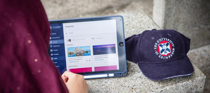 Student using tablet to browse University virtual learning environment, next to University-branded cap
