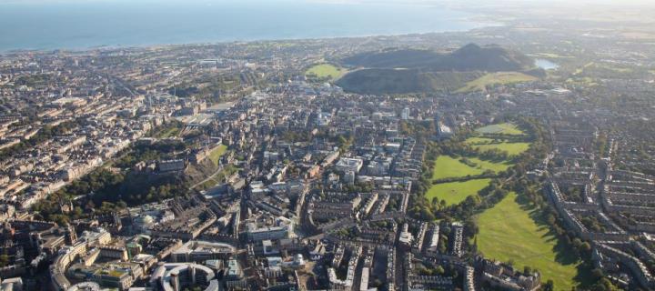 An aerial photograph of central Edinburgh showing the meadows, Bristo Square and Holyrood Park in the background