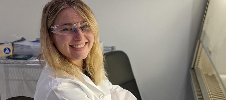 Smiling female scientist in lab, wearing white coat and protective glasses