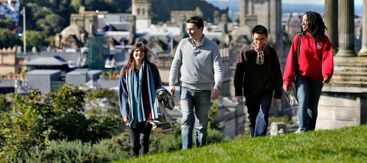 Several students walking across Calton Hill with the city in the background.