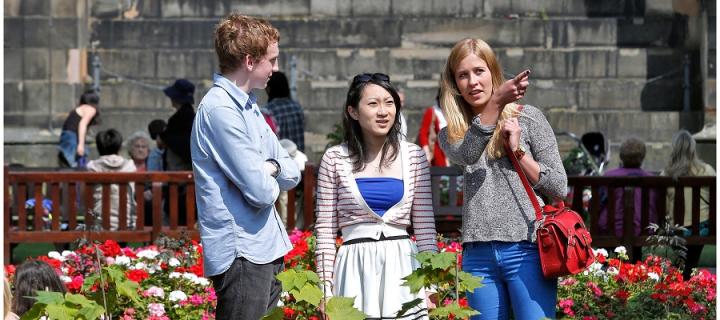 Three people stand talking and pointing in the middle of Edinburgh city.