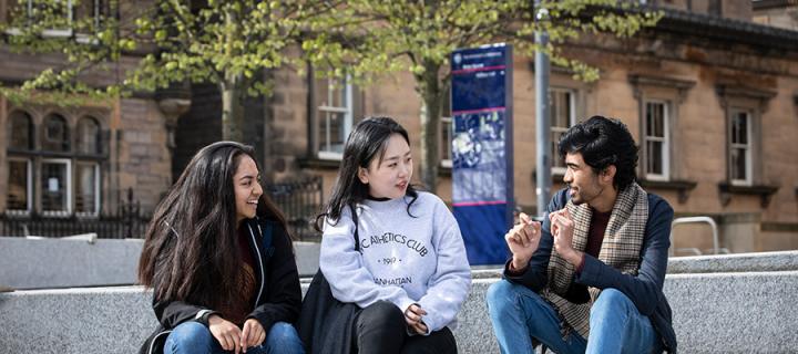 Three students sitting outside chatting