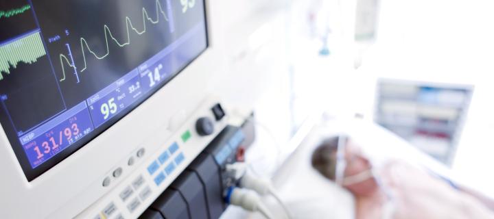 Close up of machines monitoring heart rate with man in bed in intensive care in background out of focus