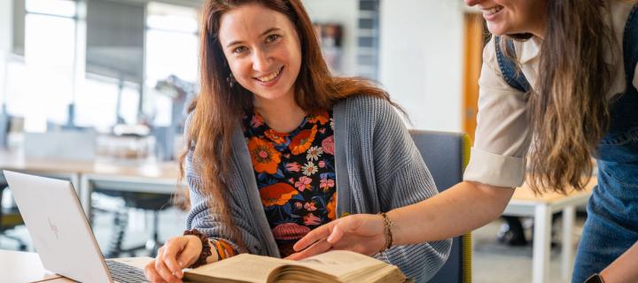 Two people discussing a Heritage Collections book that is open on the table.