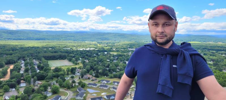 Iskandar Sattibaev smiling at the camera with green hills and forest in the background