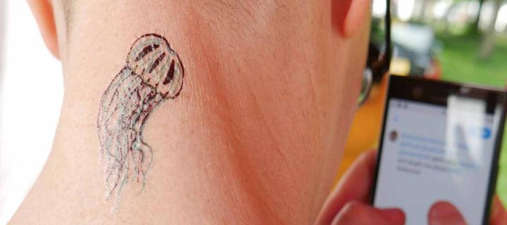 Image of back of a person holding a phone, thier neck has a temporary jellyfish tattoo. 