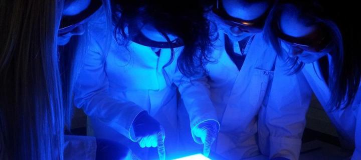 Children in dark with UV light, with goggles and lab coats, look at screen