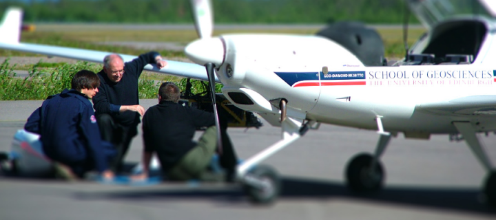 Three people under a light aircraft wing doing maintenance work 