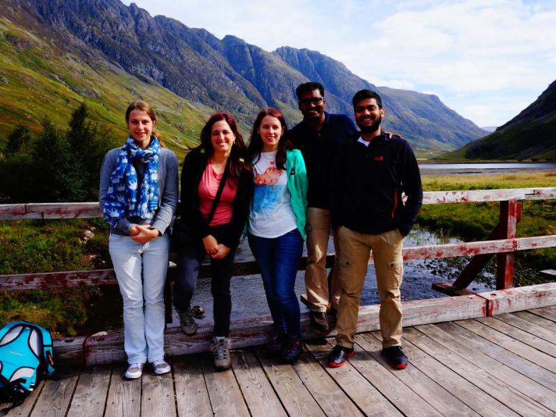 Group photo with the lab members standing on a bridge over a river, large mountains in the background