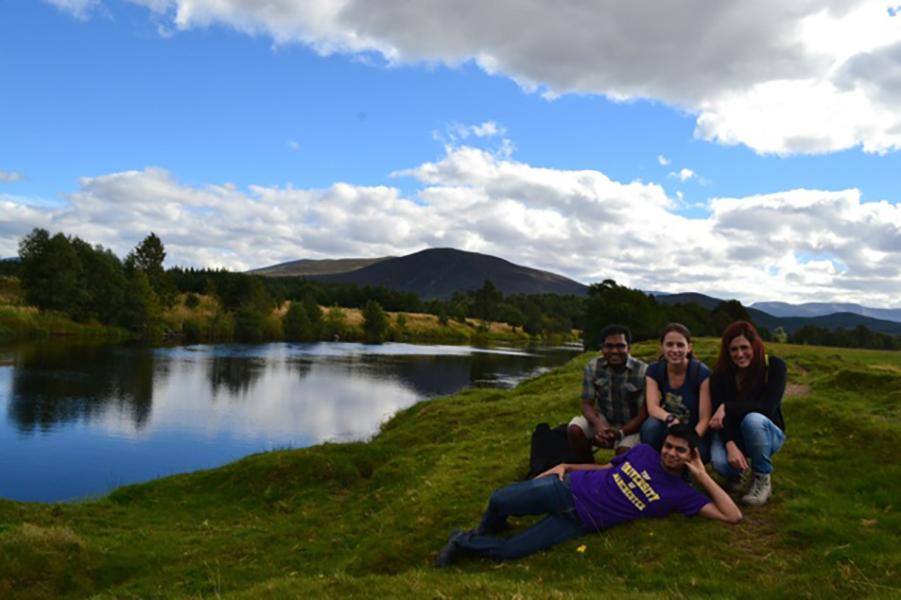 Four group members sit by a lake on a grassy slope in a wild scottish landscape