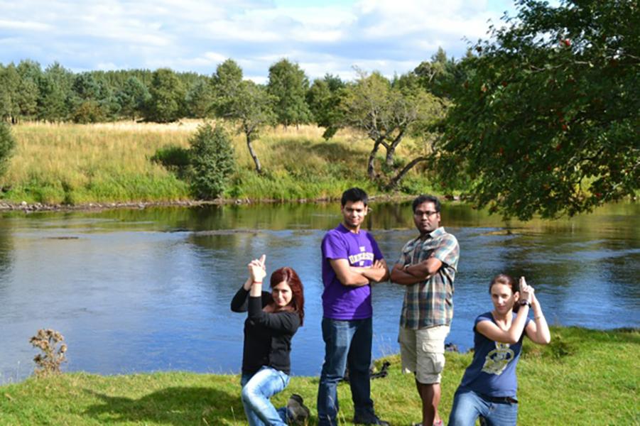 Four lab group mebers stand by a lake making Charlie's angels poses