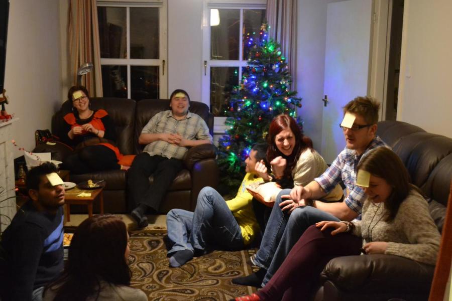 Lab group members gathered in a lounge decorated for Christmas, playing a game with post-its on their heads