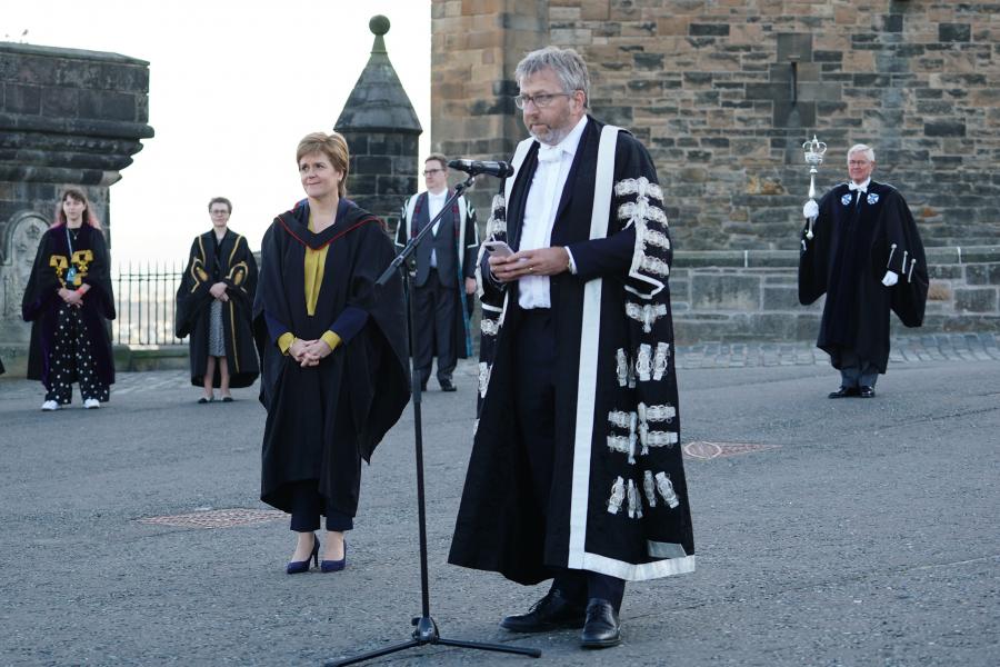 The Principal addresses the audience with the First Minister looking on