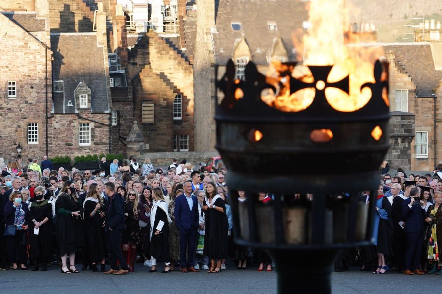 A flaming torch in the foreground with the castle and guests to the rear