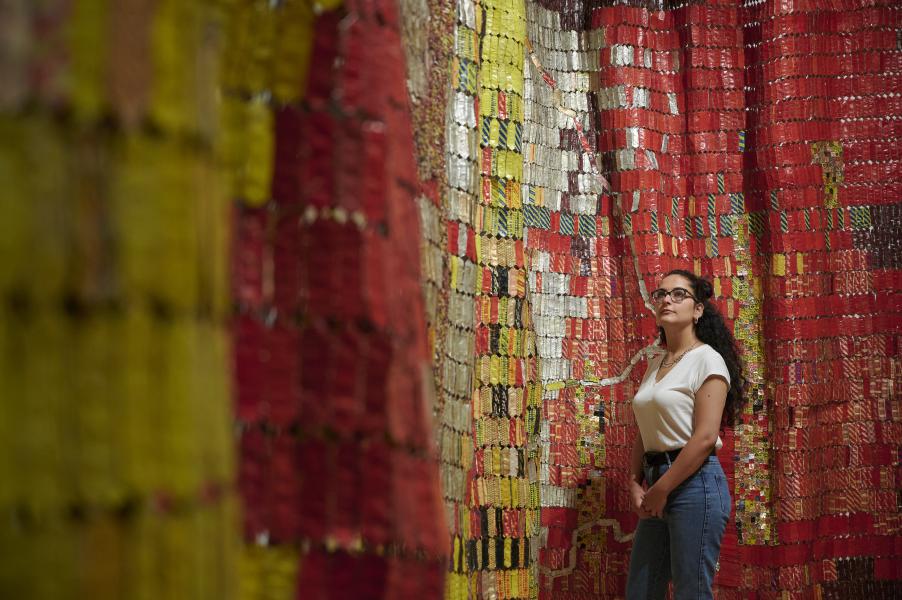 A woman standing in front of one of El Anatsui's hanging metal artworks