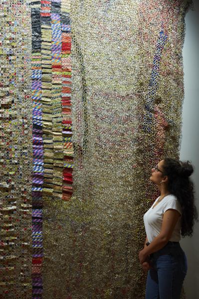 A model poses in front of one of El Anatsui's hanging metal artworks