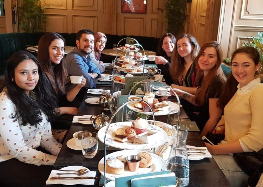 Group photo, all members sitting around a table with cups, plates and platters of cakes