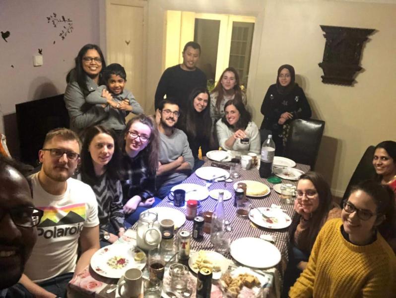 Photo of the group members sat around a large dining table eating pancakes