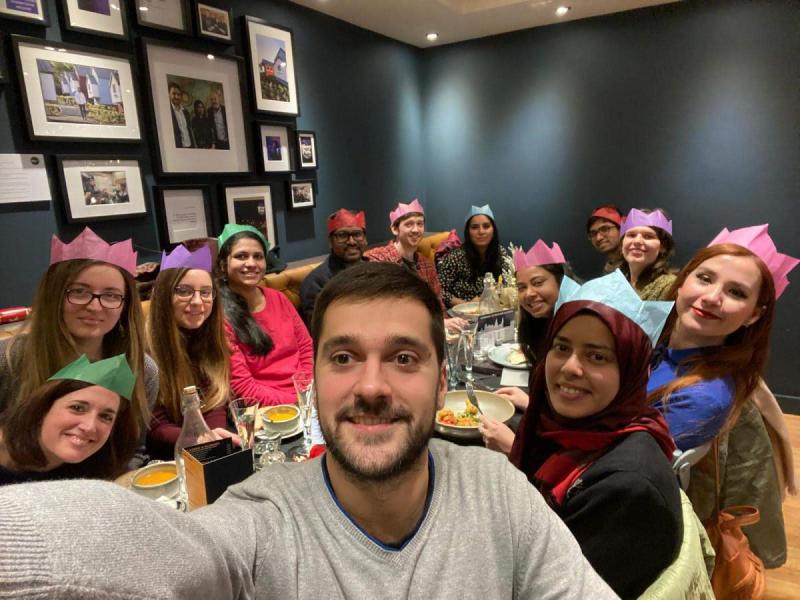 Group photo of all the lab members sitting at a table with paper crowns on