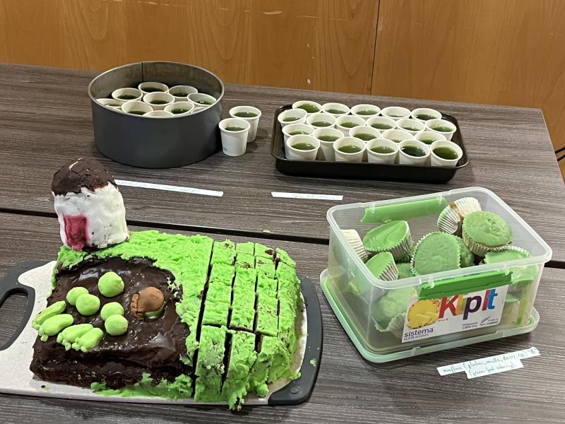 Photo of a cake with green icing, green jellies in small paper cups and cupcakes with green icing