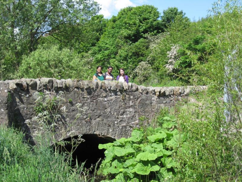 Lab group members stand on an old stone bridge surrounded by trees 