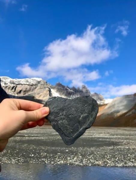 hand holding stone heart in front of beach and mountains