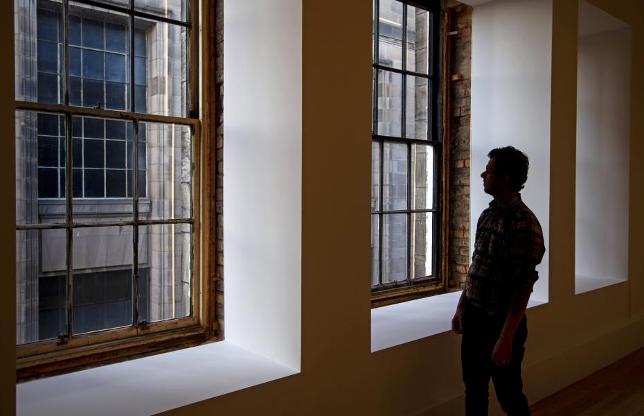 A person stands at two windows looking at pieces of art by artist Mona Yoo
