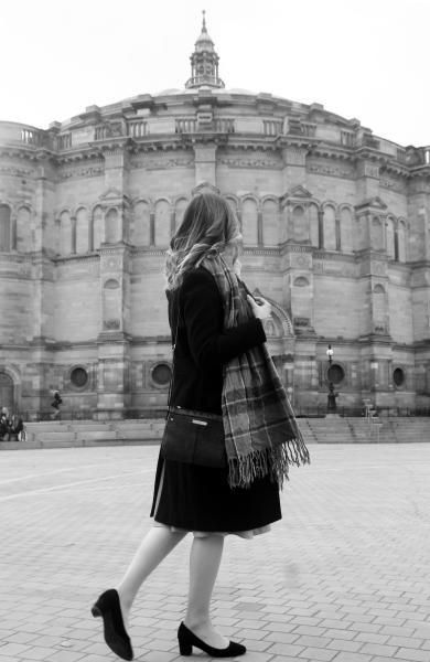 Black and white image of a woman walking in front of a large old building.