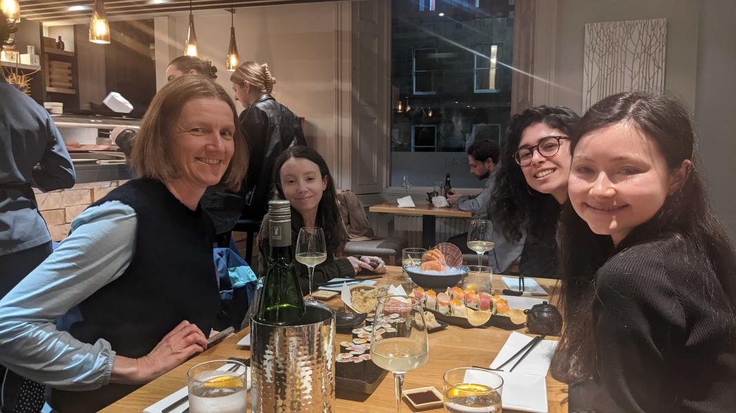 Adele and three lab members sit around a table with food and drink