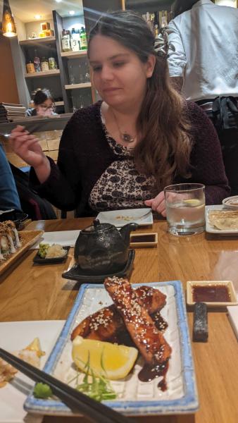 Photo of lab member sitting at a table with a tea pot and plates of sushi on it