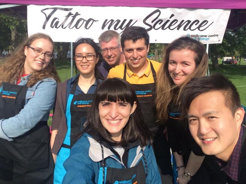 Group photo of researchers outside in front of a 'tattoo my science' banner