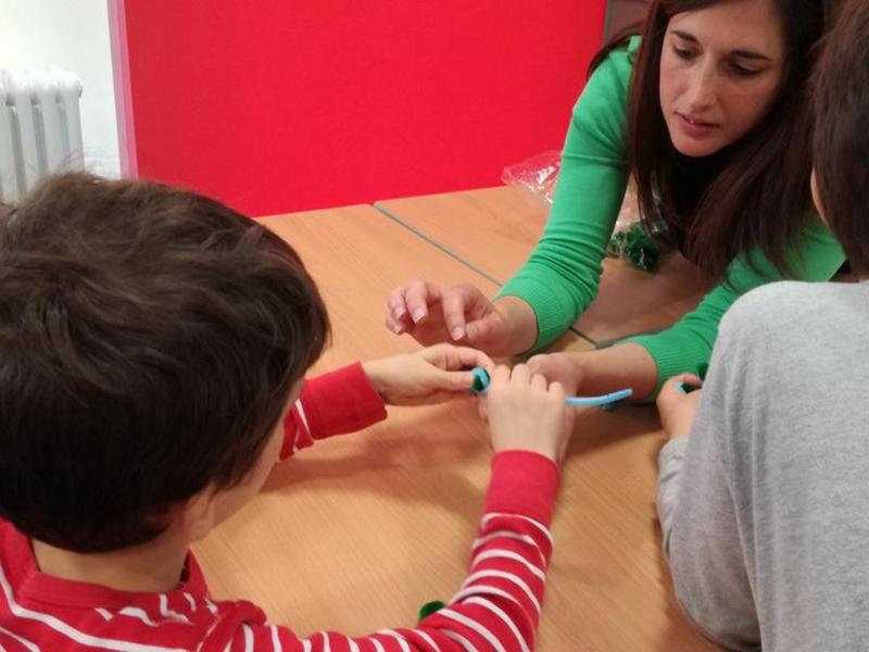 Alba reaches across a table towards a young person to show a model
