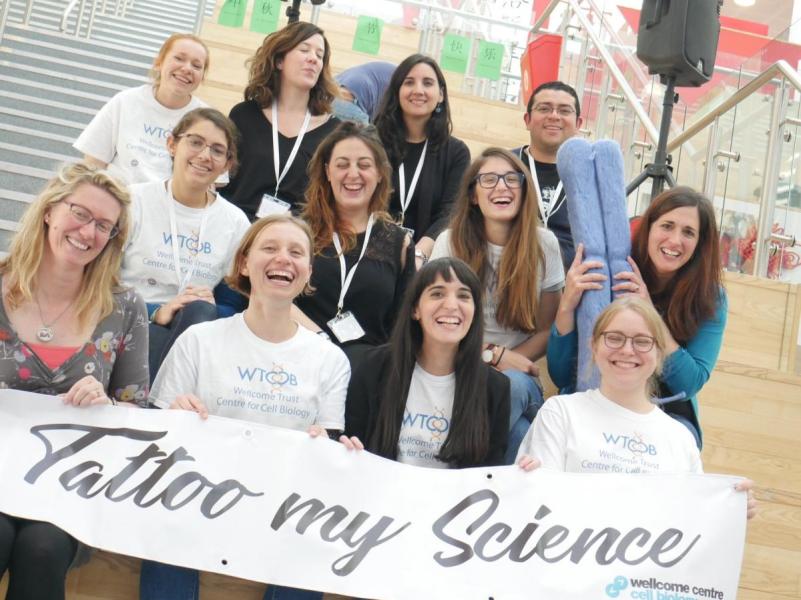 Group photo of researchers standing on steps holding a 'tattoo my science' banner