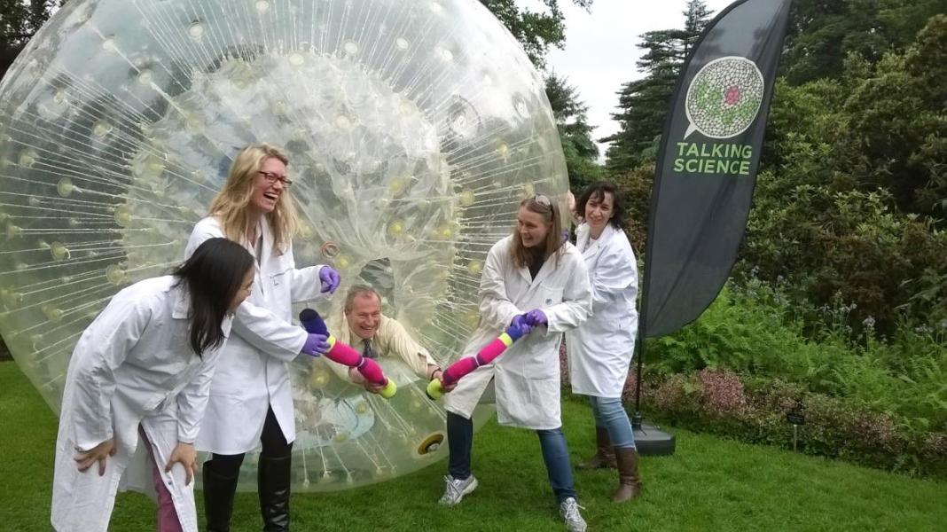 A group of researchers in lab coats stand beside the zorb ball
